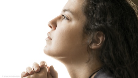 Eine Frau, im Gebet versunken, schaut nach oben.